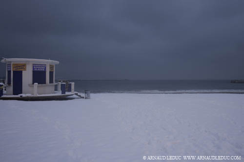 kiosque à sandwidchs rond bleu et blanc et plage des catalans à marseille recouverts de neige, en fin d'après midi, ciel nuageux gris